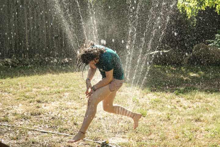 a child runs through a sprinkler in their backyard