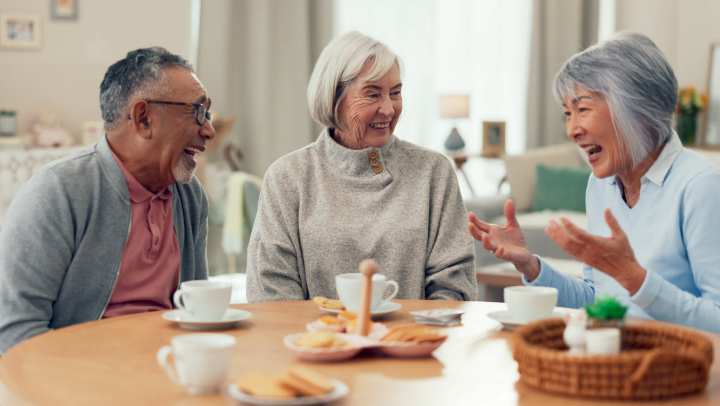 A group of people gathered in a kitchen, sharing food and drinks around a countertop with various ingredients, snacks, and kitchen items at {{location_name}} in {{location_city}}, {{location_state_name}}.