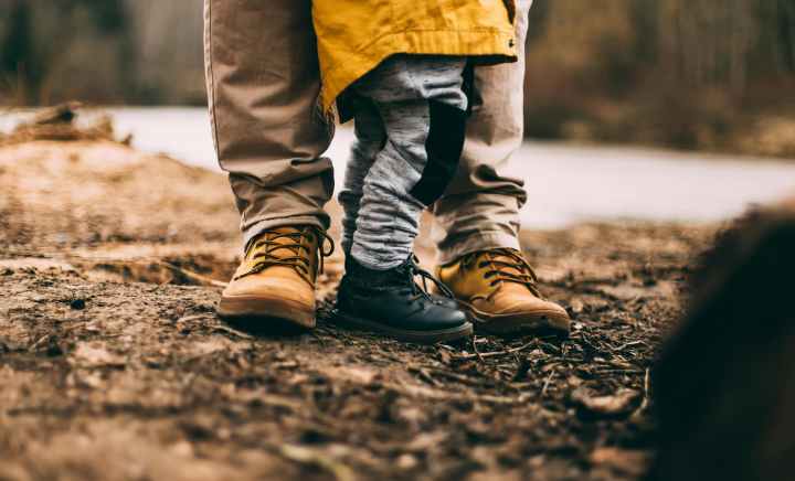 a knee down photo of a small child in hiking boots with what appears to be a father in hiking boots. 
