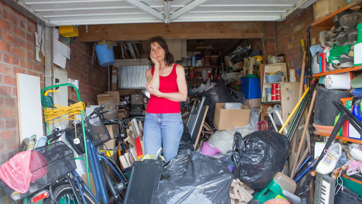 Exasperated woman standing in the middle of an overfilled, unorganized garage