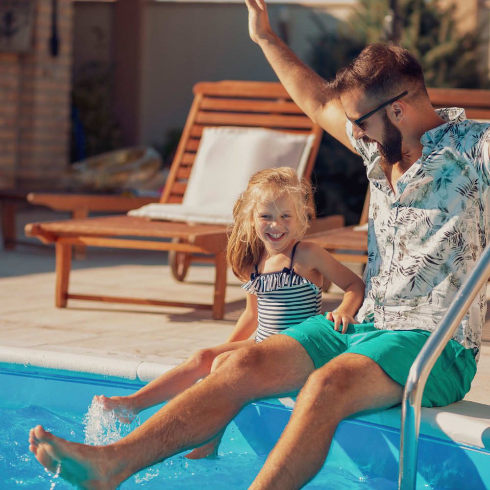 Parent and child sitting on the edge of the pool with their feet in at Tualatin View Apartments in Portland, Oregon