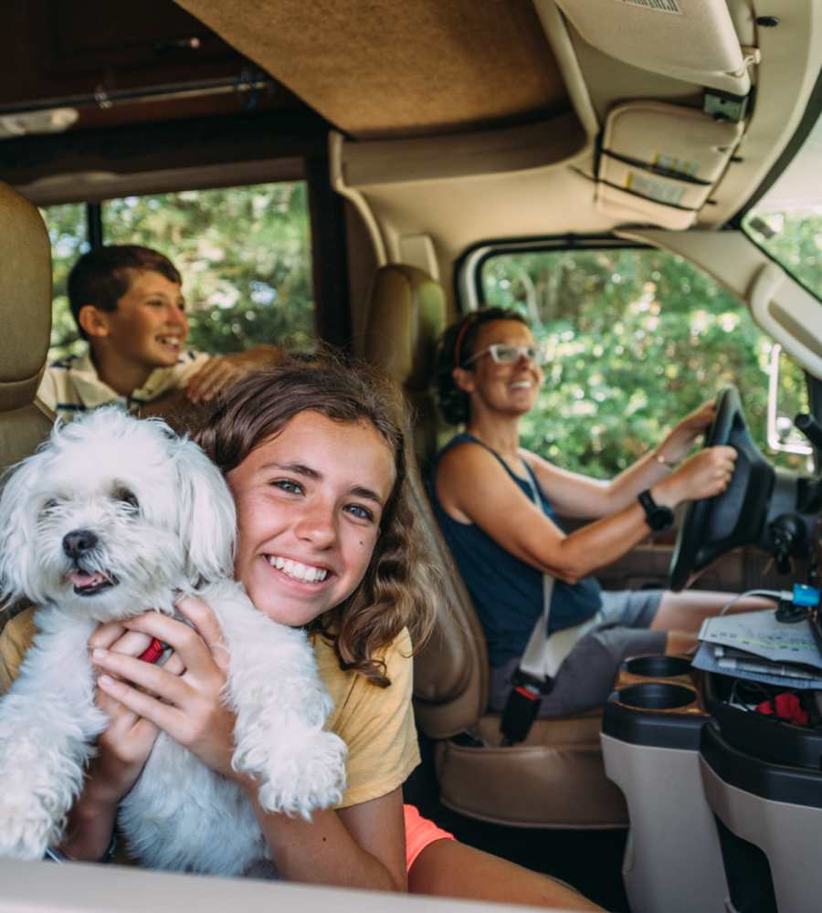 Girl holding a small dog in an RV with two smiling passengers in the front seat at Storage Authority Carolina Road in Suffolk, Virginia
