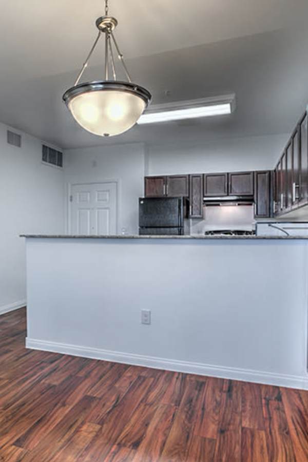 Open layout kitchen with granite countertops, stainless steel appliances, and wood-style flooring at Duet in Las Vegas, Nevada