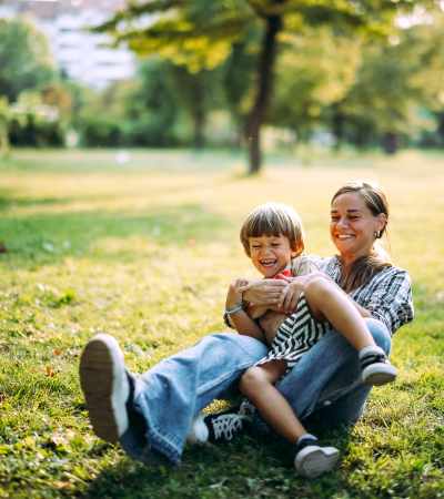 Woman sitting on grass holding smiling boy, both enjoying a sunny day in a park at Dutch Village Apartments in Baltimore, Maryland 