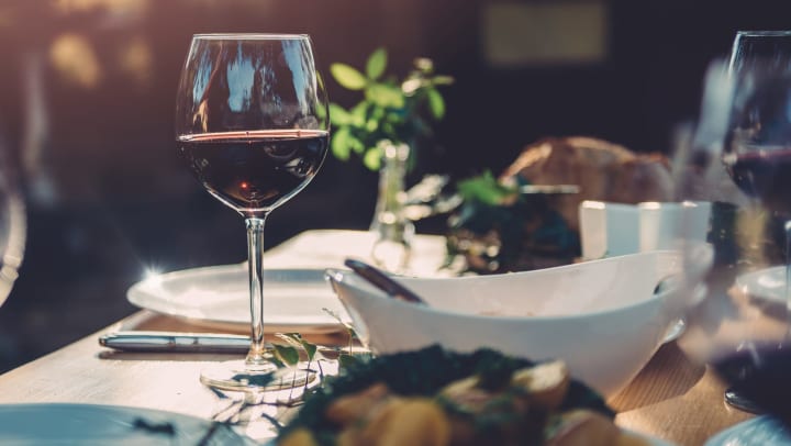 Crystal wine glasses with red wine and white ceramic plates and dishes on a wooden dining table with a roasted turkey in the background