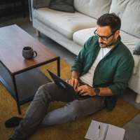 Man working on a laptop while sitting on the floor by a coffee table at South Oak in Ames, Iowa