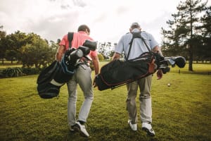 Two older men carrying golf equipment on a course near Mariposa at Reed Road in Houston, Texas