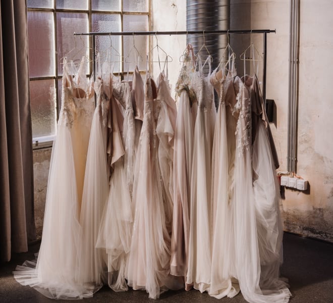 several lacy white dresses, assumed to be wedding dresses, hanging on a clothing rack