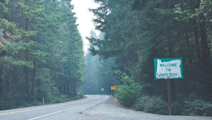 Welcome to Oregon sign and road surrounded by pine trees | Photo by Everett McIntire on Unsplash