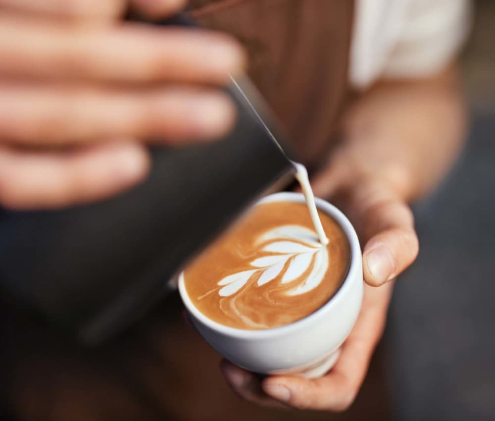 Barista pouring latte art into a white cup in a cozy café setting at South Oak in Ames, Iowa