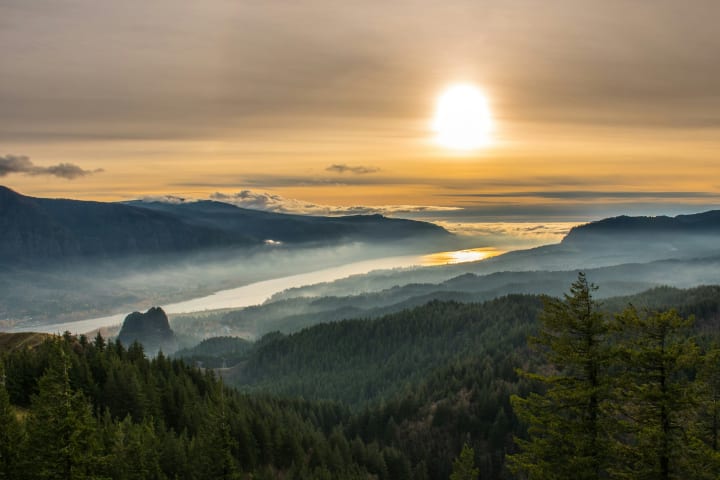 a view of the Columbia river gorge at sunrise with a hazy fog over the river and hills still