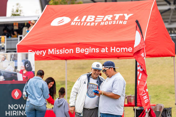Liberty Military Housing's booth pictured at the San Diego FC game with two San Diego FC fans standing in front of it