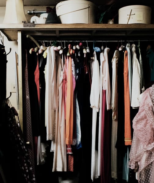 an organized closet with hanging clothes and storage boxes on a shelf above