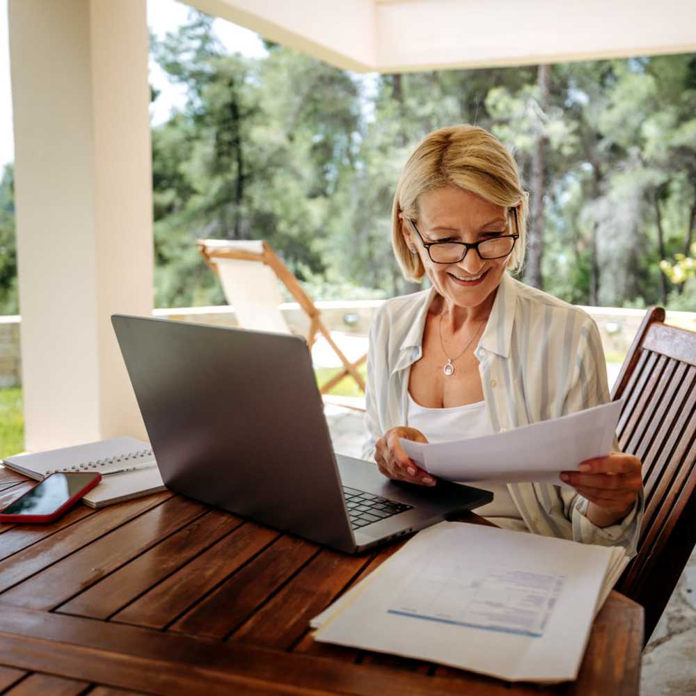 Woman working on a laptop at a wooden table outdoors, surrounded by greenery at Lindbergh Parc Senior Apartments in Fort Worth, Texas