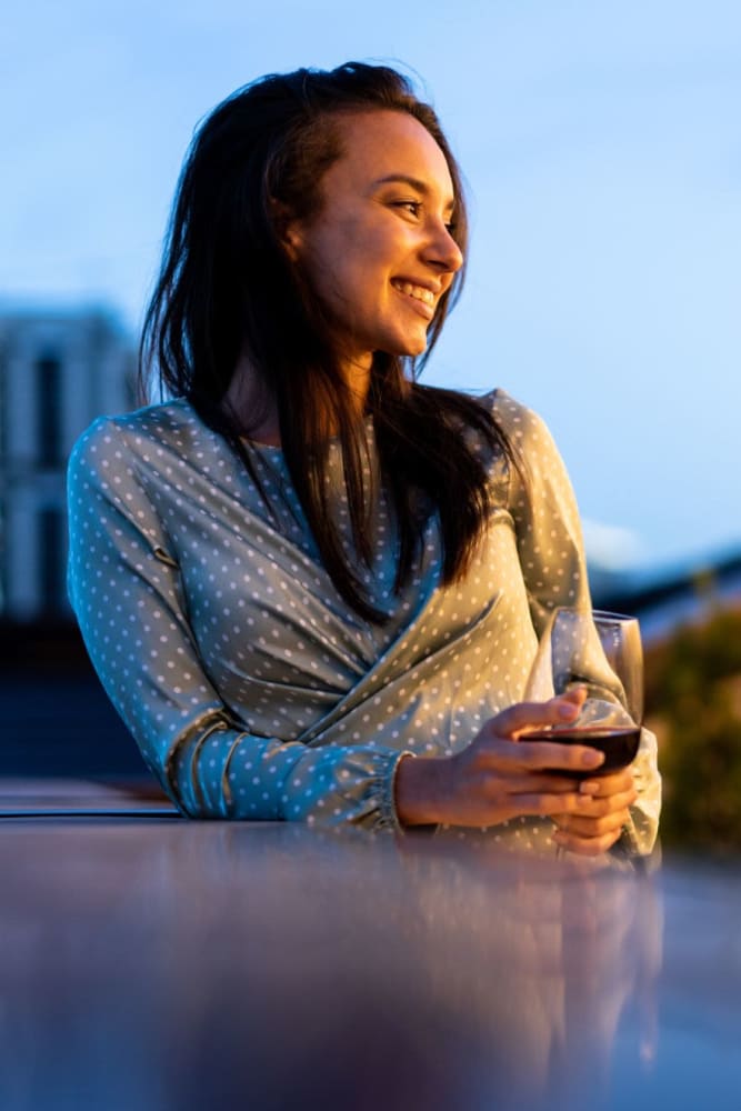 A resident enjoying a glass of wine on the rooftop terrace at 55 Brighton at Packard Crossing in Boston, Massachusetts