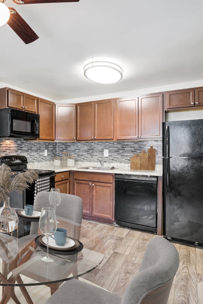 Kitchen with espresso cabinets and black appliances, next to a staged dining nook with ceiling fan at Mapleton Square Apartment Homes in Dover, Delaware