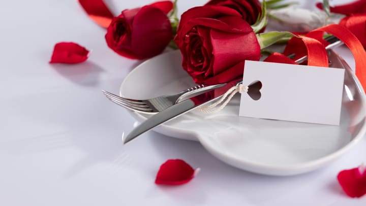 Table setting with red roses and red ribbon on a white plate with a seating card. 