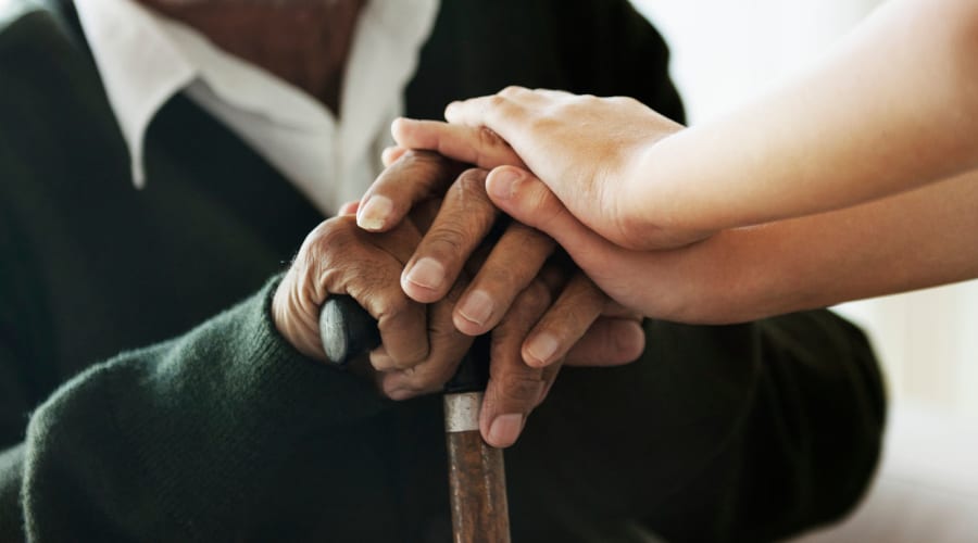 Resident resting his hands on a cane with caregiver's hands on top at Peoples Senior Living in Tacoma, Washington