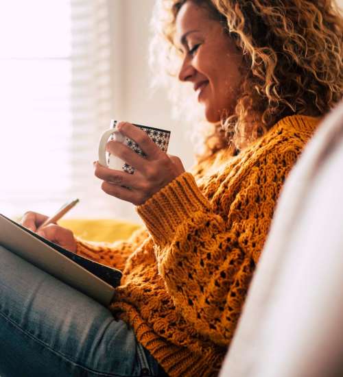 A woman on a couch enjoys a cup while writing in her living room at EVOQ East Cobb in Marietta, Georgia
