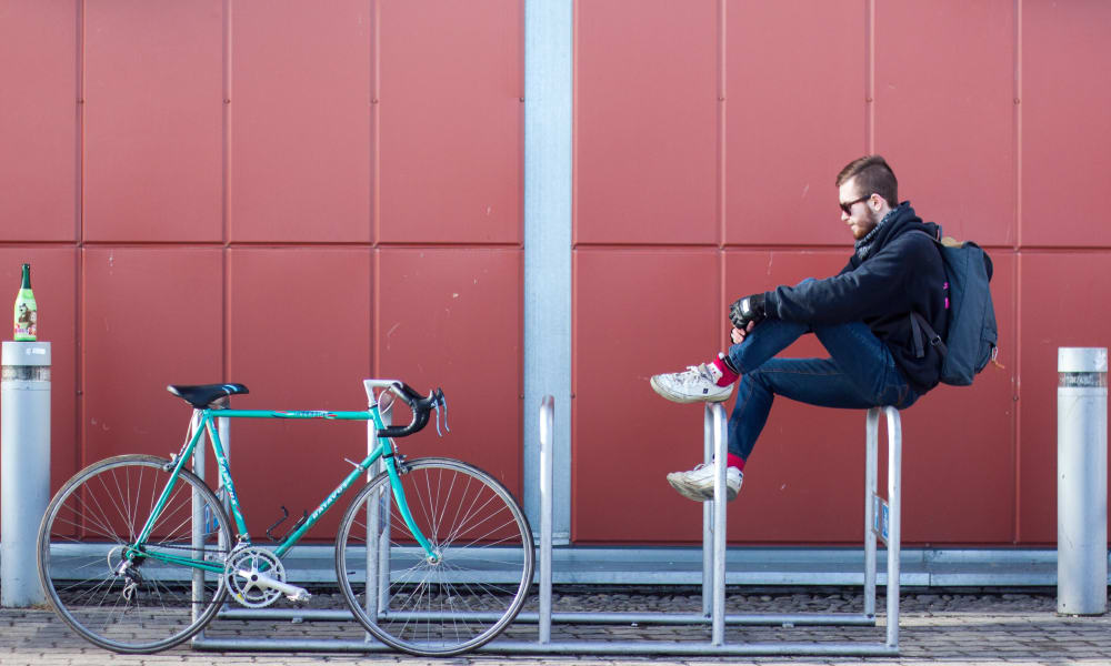 Man sitting on a bike rack next to his bike near Telegraph Arts in Oakland, California