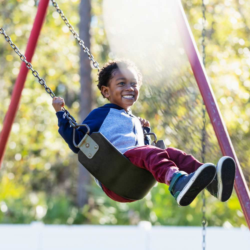 A young boy happily swinging on a swing in a playground at Taft Terrace in Taft, Texas