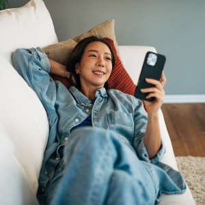 Woman relaxing on couch with smartphone at Penn Lincoln Apartments in Wilkinsburg, Pennsylvania