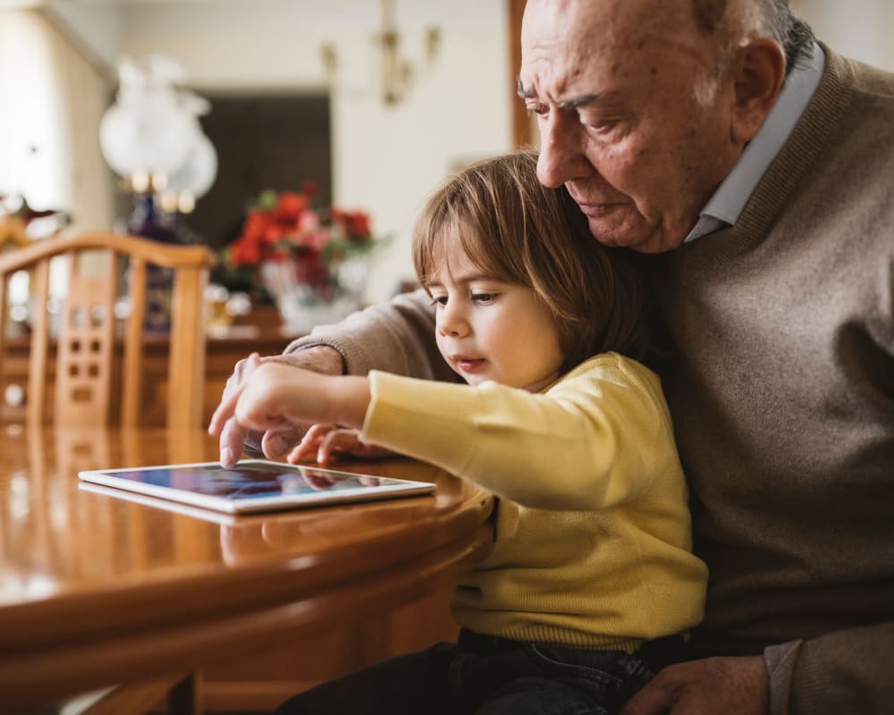 Grandfather and his grandchild playing on a tablet in the dining room at The Pillars of Prospect Park in Minneapolis, Minnesota