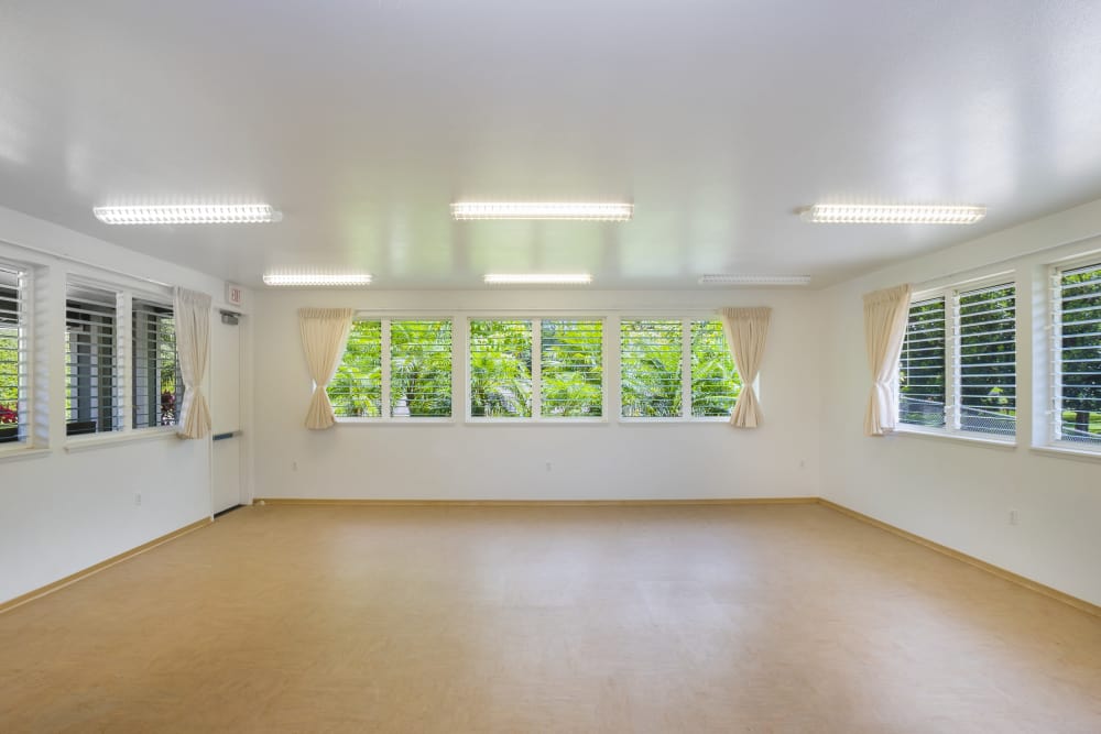 A spacious, well-lit room with light wood flooring, surrounded by large windows with beige curtains at Pa'anau Village II in Koloa, Hawaii