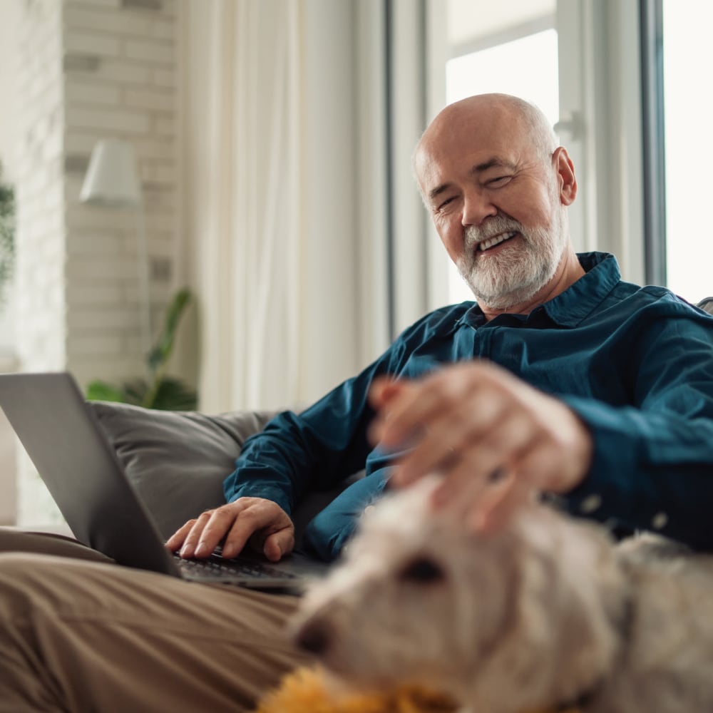 A resident petting his dog and working on his laptop at Lakeview Terrace of Boulder City in Boulder City, Nevada