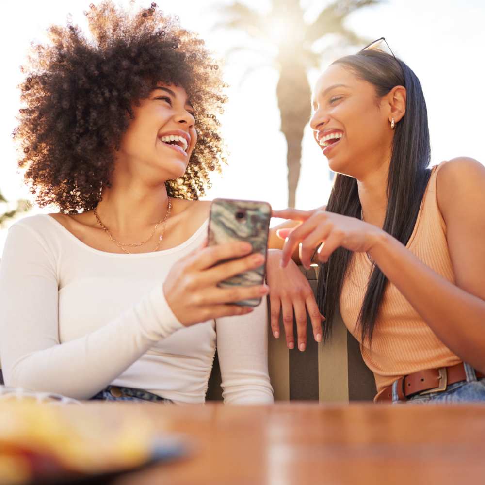 Two smiling residents looking at a phone outside at DECRO Long Beach in Long Beach, California