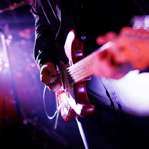 Guitar being played on stage under vibrant purple and pink concert at Titan Court in Eugene, Oregon