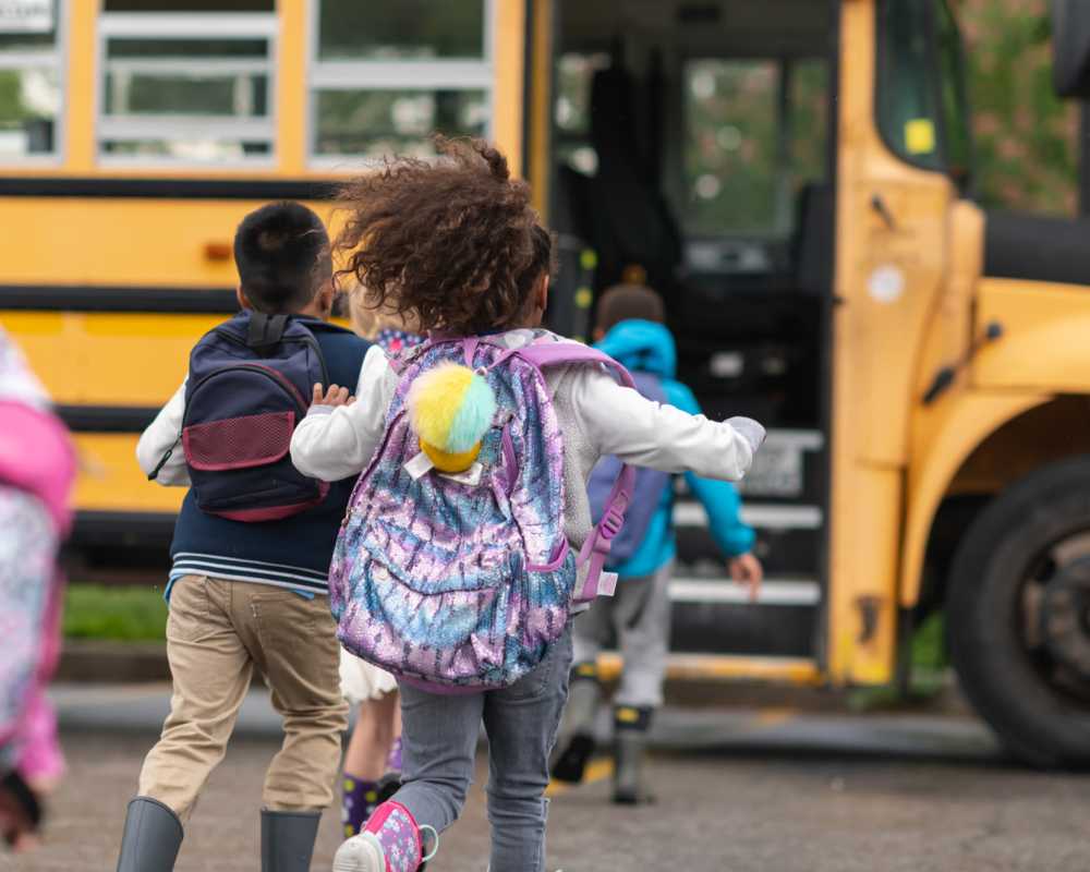 Children joyfully running to school as a school bus waits nearby Ansley Murrayhill in Tigard, Oregon