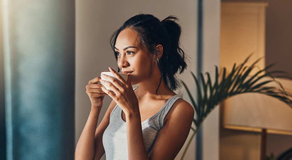Woman looking out the window while having a cup of coffee in her home at Ruby Vista in Denver, Colorado