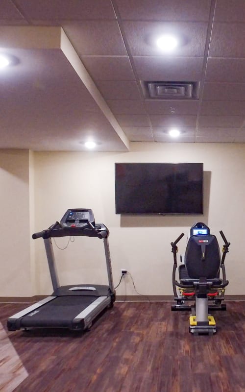 Community fitness room with cardio equipment and large wall mounted television at The Pillars of Mankato in Mankato, Minnesota