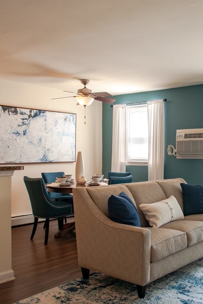 Open layout living room and connecting dining room with hard-wood style flooring and plenty of room for a couch and more at Hill Brook Place Apartments in Bensalem, Pennsylvania