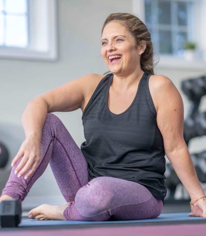 A woman is seated on a gym mat, preparing for her exercise routine at EVOQ East Cobb in Marietta, Georgia