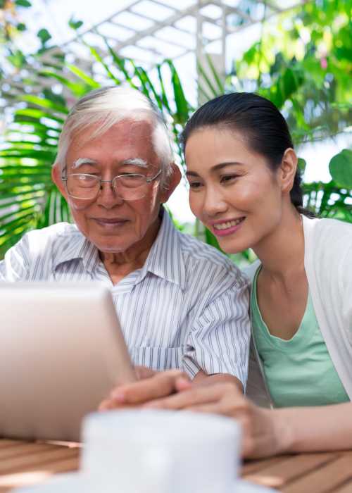 Father and daughter learning about assisted living communities on a tablet near The Pineapple House at Sapphire Lakes in Naples, Florida