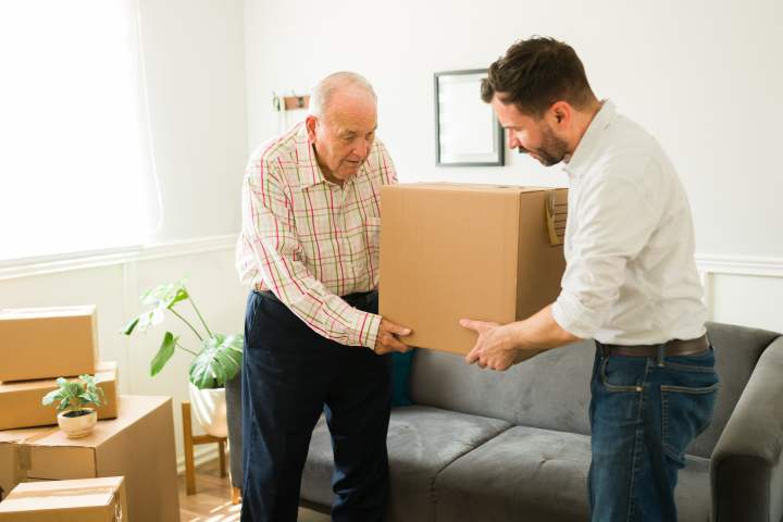 A caring son helps his elderly father with moving boxes, working together to prepare for a transition to senior living.