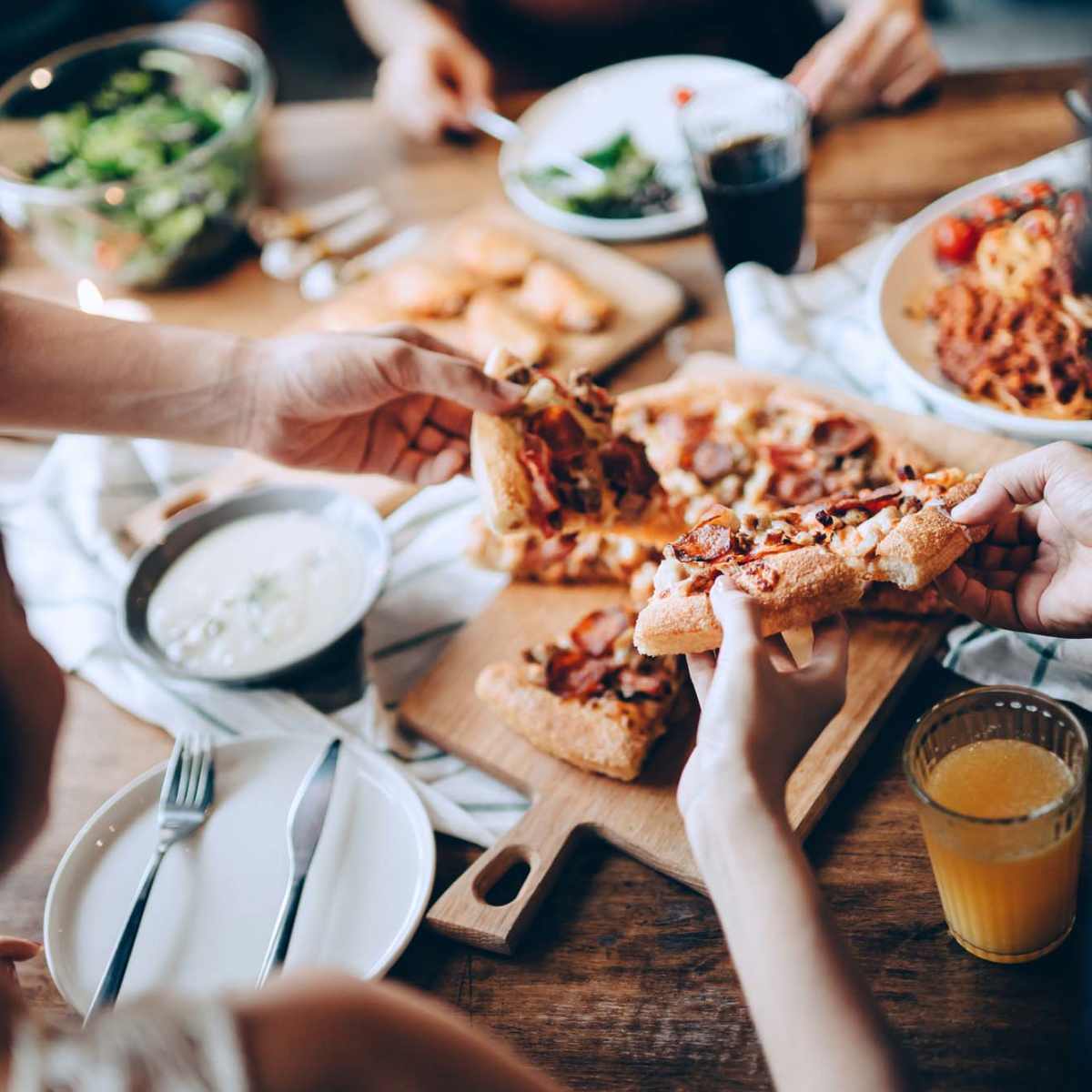 People sharing pizza at a wooden table with salad and drinks nearby at Stevens Creek Commons in Augusta, Georgia 