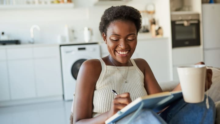a young woman sitting in her kitchen checks items off a to-do list | important year-end tasks