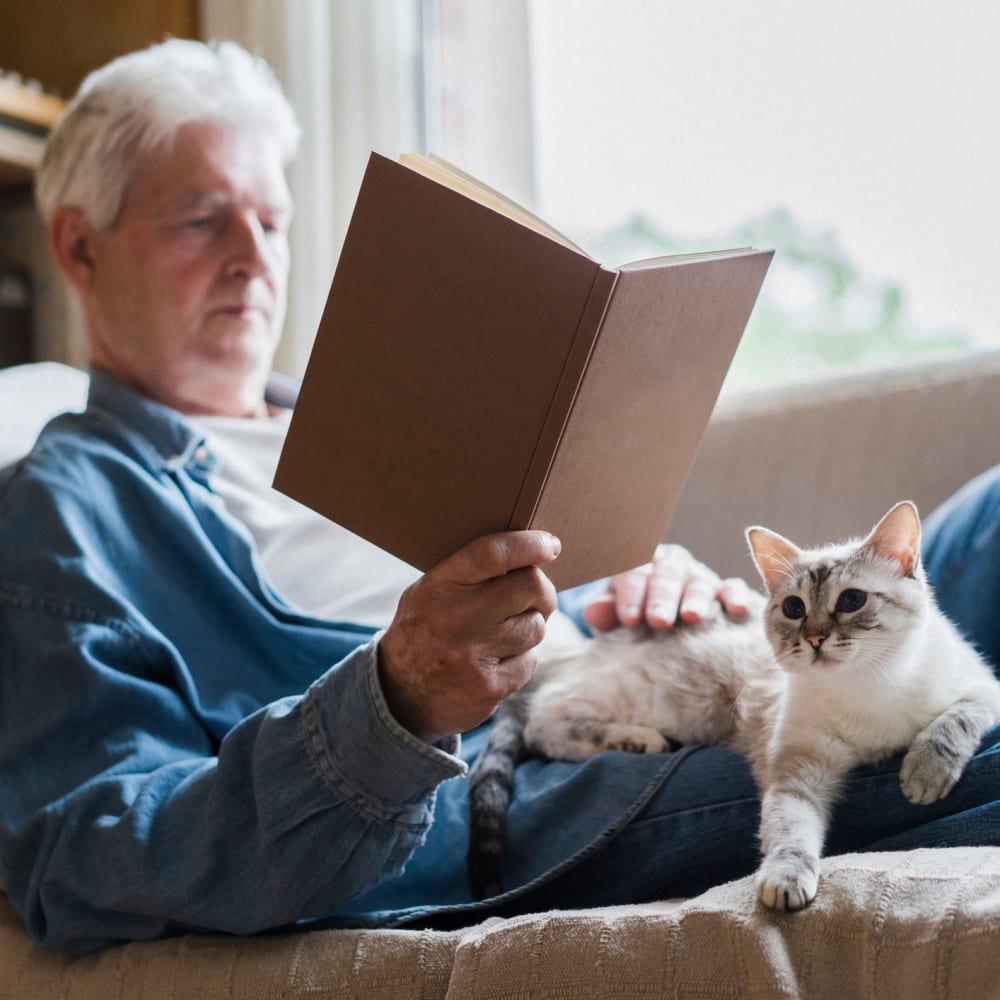 A resident reading a book with a cat in his lap at Garden Square at Westlake Assisted Living in Greeley, Colorado