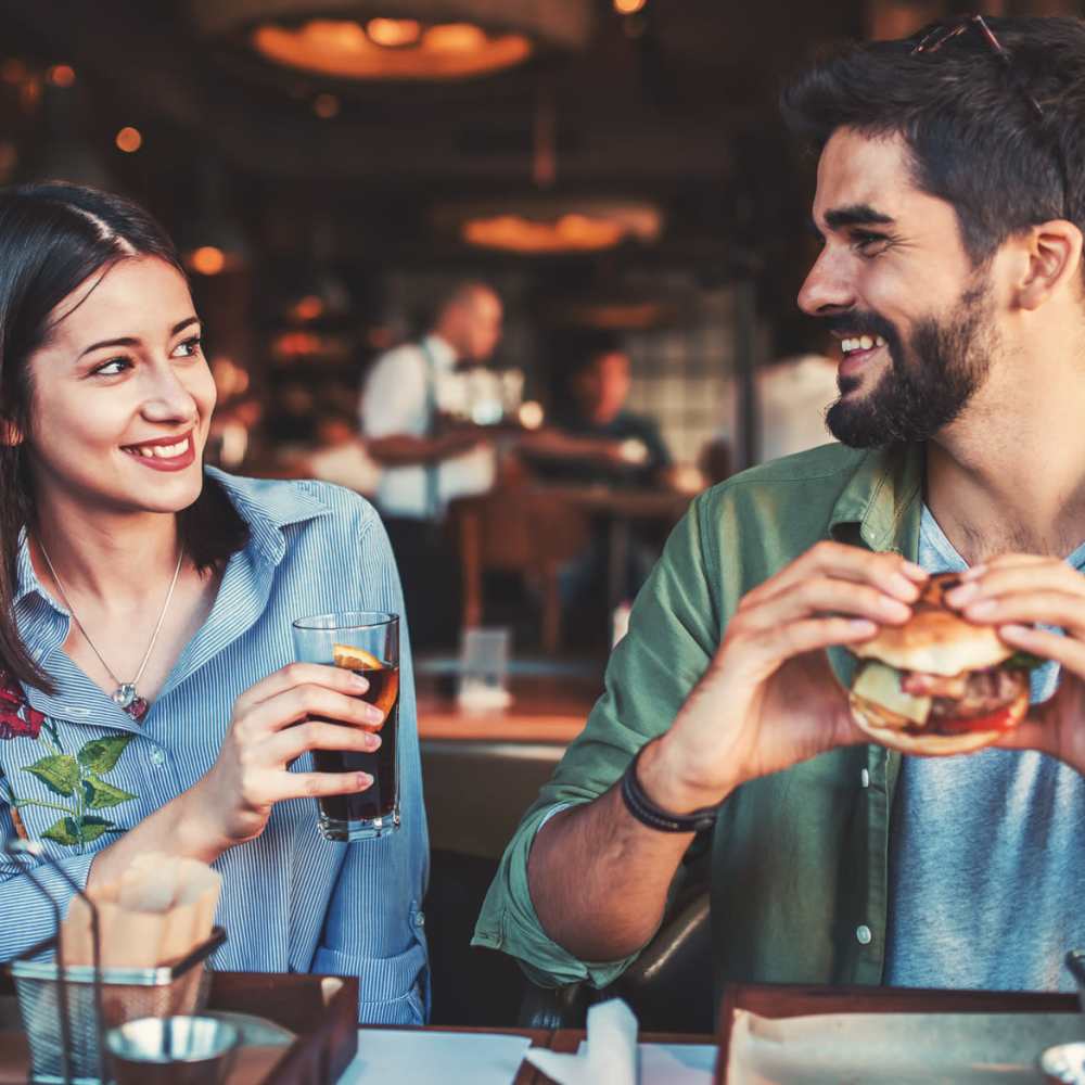 A couple sitting at a restaurant table, happily eating burgers and enjoying each other's company near Gateway Commons in Hillsboro, Oregon