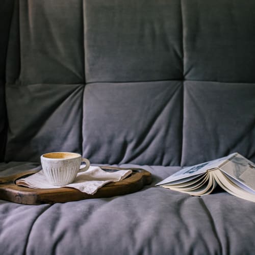 A cup of coffee and a book on a couch at Vesta Creeks Run in North Charleston, South Carolina