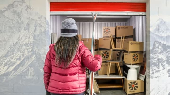 Woman in winter clothing, holding skis, while standing in front of her StorQuest storage unit, filled with StorQuest boxes.