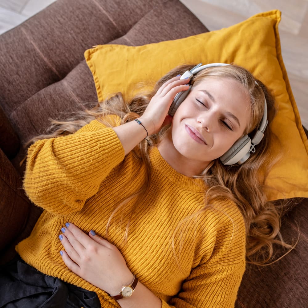 Resident laying back on the couch jamming to her favorite tunes with headphones on at Campbell Flats Apartments in Springfield, Missouri