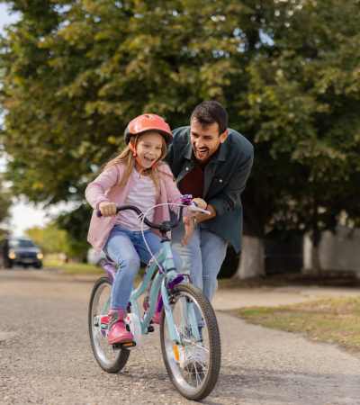 Father encouraging daughter riding bike outdoors near Clarkwood Greens in Warrensville Heights, Ohio