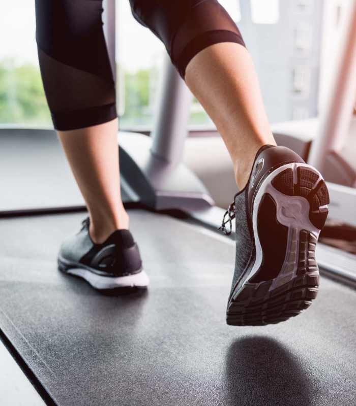 Woman jogging on a treadmill, wearing athletic leggings and shoes, focused on fitness at Rincon Apartments in McAllen, Texas