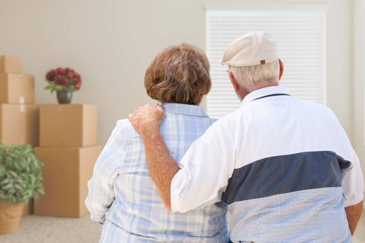 A senior couple embraces while looking at packed boxes, preparing for their exciting move to a welcoming senior living community.