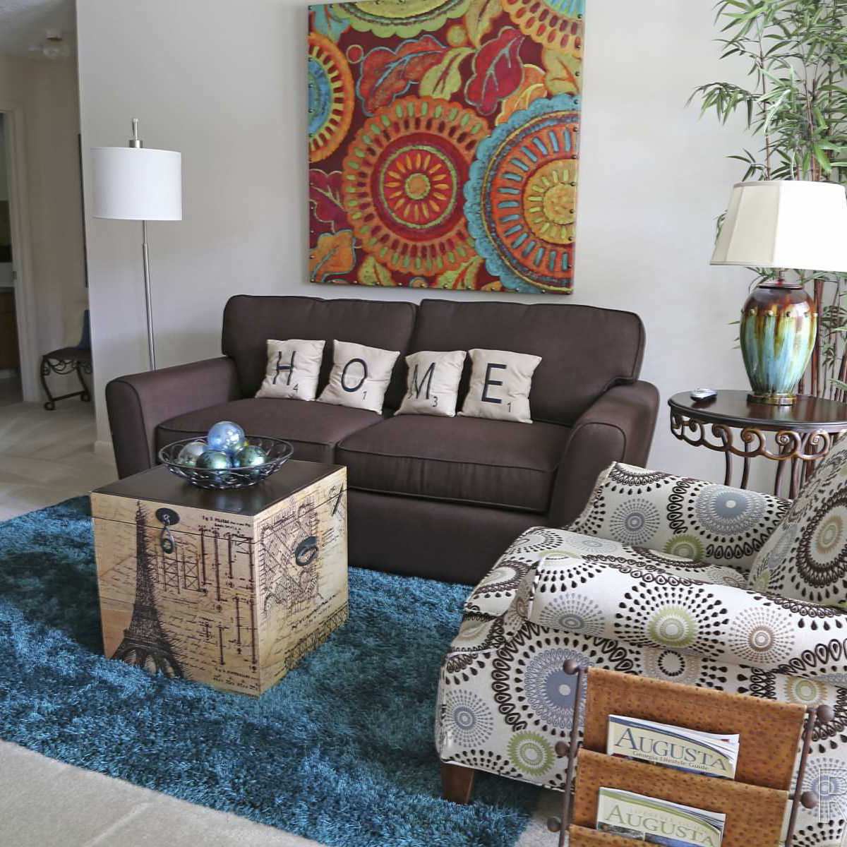 Cozy living room with brown couch, decorative pillows, colorful artwork, and stylish accent chair at Stevens Creek Commons in Augusta, Georgia 