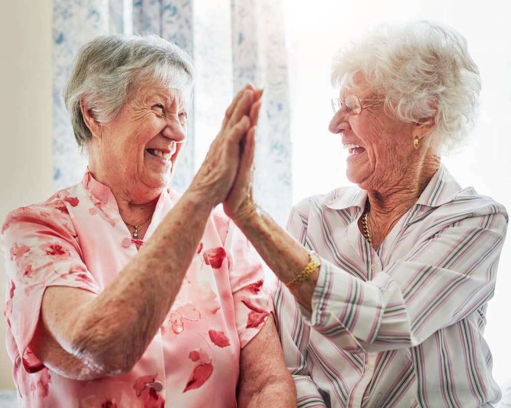 Two residents smiling and giving each other a high-five at Milestone Senior Living Eau Claire in Eau Claire, Wisconsin. 